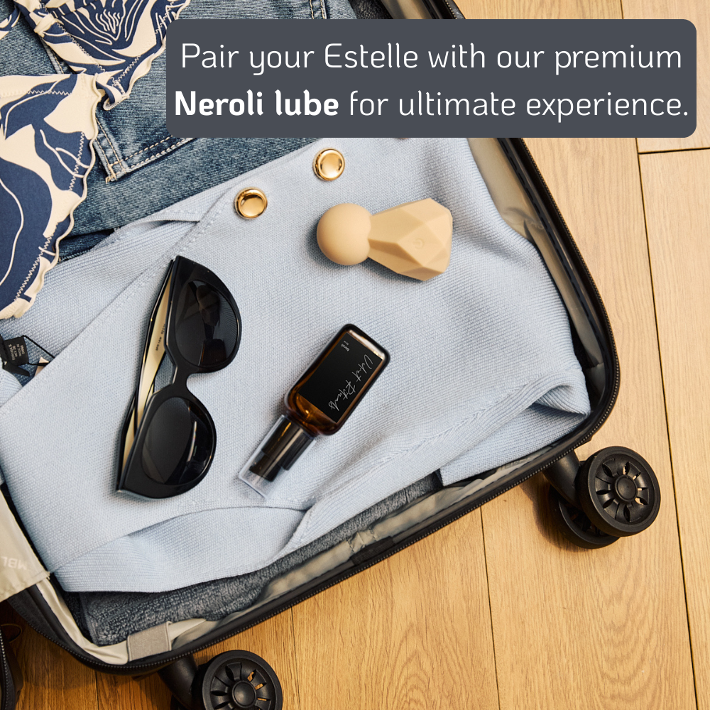 Velvet Rituals Estelle compact massager paired with Neroli premium lubricant, shown as a travel-friendly lifestyle flat lay inside a suitcase