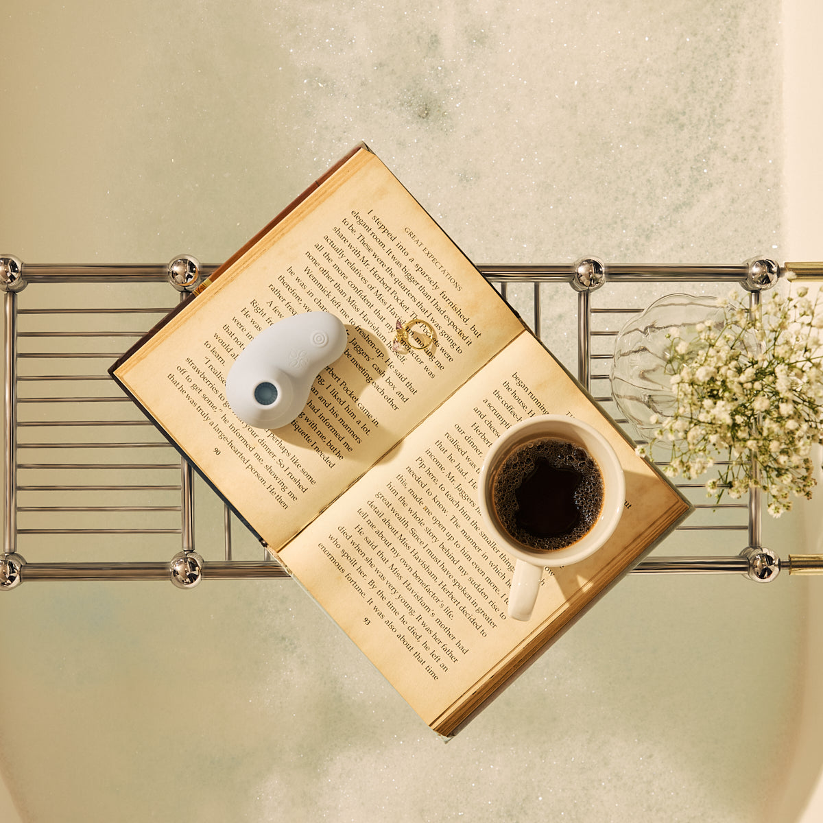 Velvet Rituals Aurora air suction massager placed on an open book beside a cup of coffee, styled as a calm lifestyle setting