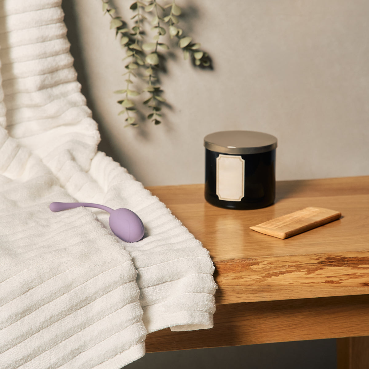 Velvet Rituals Pearl internal massager resting on a folded towel beside a candle, representing a calm, spa-like self-care setting