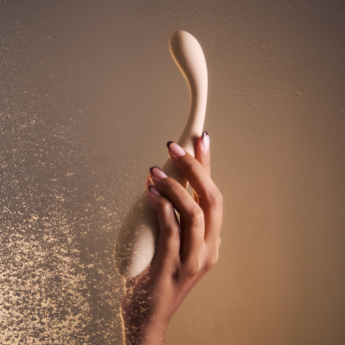 Hand holding Velvet Rituals Celeste ergonomic massager against a warm, softly textured background, highlighting its elegant curved design