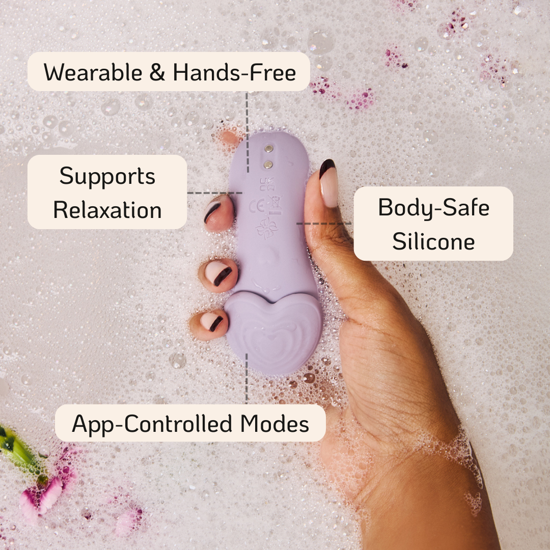 Velvet Rituals Whisper wearable personal massager highlights. Hand holding the massager in the water with flower petals.